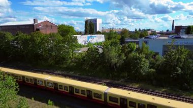 Güneşli bir yaz gününde Berlin, Almanya 'da Tempelhofer Feld' den geçen sarı bir S Bahn treninin hava görüntüsü. İHA yükseliyor 