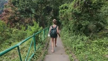 Bereketli tropikal bir ormanda taş merdivenlerden inen bir kadın turist görüntüsü.