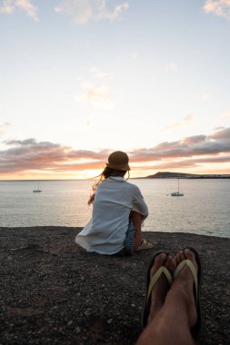 Sahilde bir kadının arka görüntüsü, sakin bir akşamda sakin bir günbatımını ve uzak bir tekneyi hayranlıkla seyrediyor..