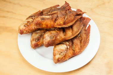 Lezzetli kızarmış balık, beyaz bir tabakta tilapia; ahşap arka plan üzerinde fotoğraf
