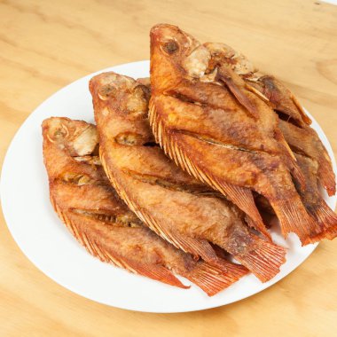 Lezzetli kızarmış balık, beyaz bir tabakta tilapia; ahşap arka plan üzerinde fotoğraf