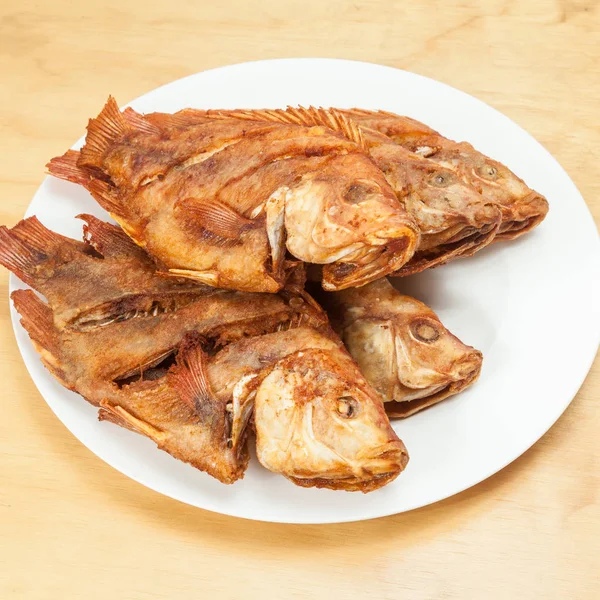 Lezzetli kızarmış balık, beyaz bir tabakta tilapia; ahşap arka plan üzerinde fotoğraf