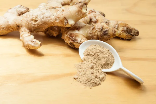 Fresh roots and ginger powder - Zingiber officinale; photo on wooden background