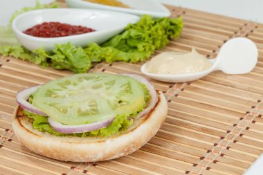 Sebzeli hamburger için bir dilim ekmek: Yeşil domates, marul ve soğan halkaları; Burger 'i birleştirmeye hazır.