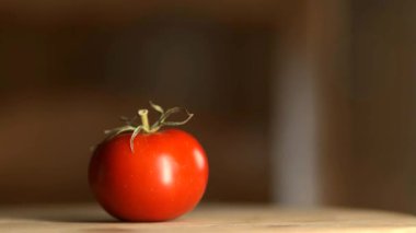 Tahta yüzeyde dönen yeşil saplı taze kırmızı domates, bulanık arka planda izole edilmiş, doğal parlaklığı ve canlı rengi gösteriyor..