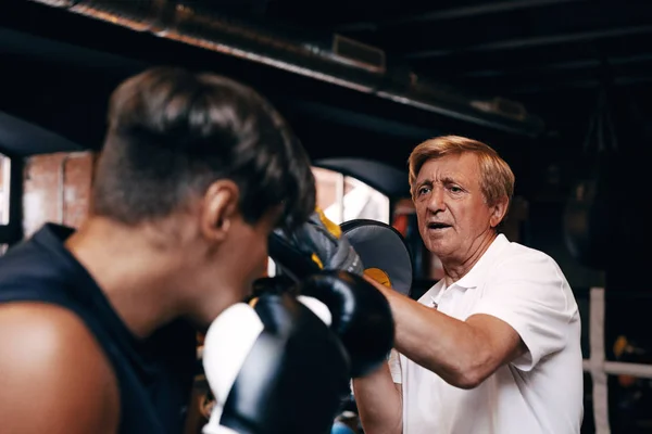 Male coach teaching boxer at health club. Two people exercising indoors.