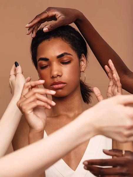 Beautiful young woman posing with unrecognizable females hands near her face against a brown background
