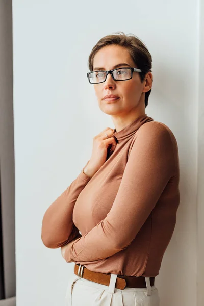 Portrait of a businesswoman in formal wear standing at wall. Female wearing eyeglasses looking away.
