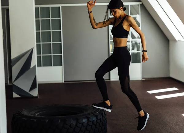 Young muscular woman doing steps in gym using a big tire