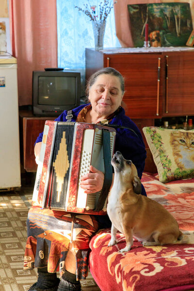Eastern Europe, Ukraine, Pripyat, Chernobyl. Returned resident of Chernobyl, female, known as The Babushkas. Playing accordian with her dog. In her apartment. April 11, 2018.