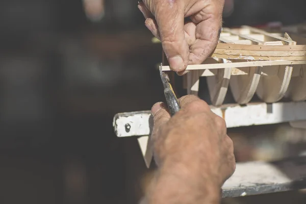 old man working on creating a wooden model of a boat