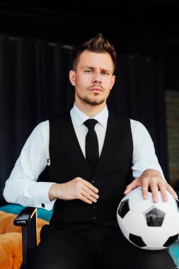 Bir takım elbise ve bir futbol topu şık spor adamı. Bir çatı duvar arka planı.