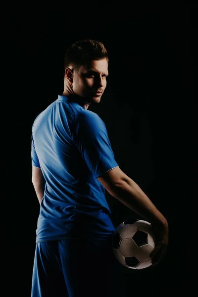 Młody piłkarz z piłką na czarnym tle w studio. — Zdjęcie stockowe