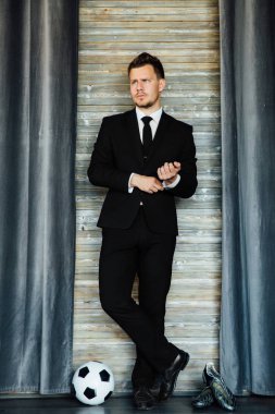 Bir takım elbise ve bir futbol topu şık spor adamı. Bir çatı duvar arka planı.