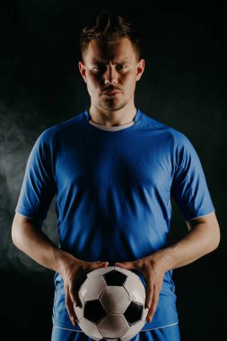 Young soccer player with ball on black background in studio. clipart