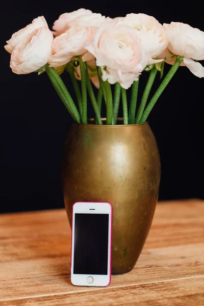 Bouquet virágok rózsaszín finom Boglárkák áll egy fából készült asztal arany vázában. — Stock Fotó