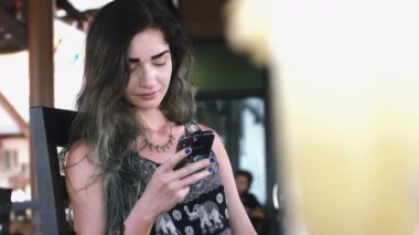 Sokakta bir kafede güneşli gün boyunca telefonla yazarak güzel genç kadın.