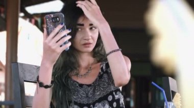 Sokakta bir kafede güneşli gün boyunca telefonla yazarak güzel genç kadın.