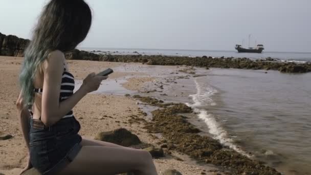 若い観光女の子を使用して携帯電話に美しいボートで海の近くのビーチ . — ストック動画