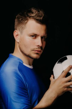 Yakın çekim portre genç yakışıklı futbol oyuncu futbol koyu arka plan üzerinde poz.