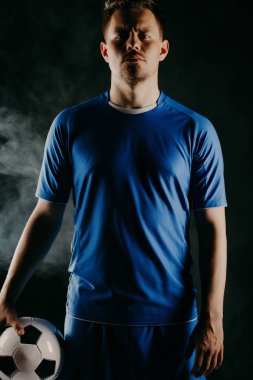 Young soccer player with ball on black background in studio. clipart