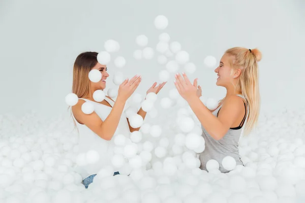 Retrato Happy Girlfriends parada rodeada de bolas de plástico blanco en la piscina seca . — Foto de Stock
