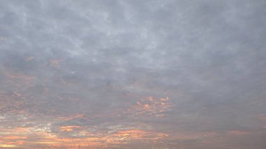 Karanlık bulutlardan bir battaniyeyle gün doğumu gökyüzü. Güneş sadece ufukta görünür. Canlı turuncu ve sarı bir parıltı yayar. Bulutların altını aydınlatır ve dramatik bir sahne yaratır..