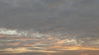 Şafak vakti gökyüzünün dramatik geniş açılı görüntüsü. Üst yarıyı yoğun gri ve koyu bulutlar kaplarken, alttaki güneş doğarken ortaya çıkan turuncu ve pembeyle aydınlanıyor..
