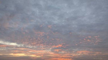 Gri bulutlarla kaplı bir battaniyeyle çarpıcı bir gündoğumu gökyüzü. Görüntünün alt kısmı parlak, turuncu ve kırmızı bir parıltıyla aydınlanır..
