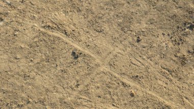Toprak ve kum zemininin tepeden tırnağa görüntüsü. Yüzey lastik izleri ve ince çizgilerle desenli, ve birkaç küçük kaya ve toprak yığını görülebilir, soyut, doğal bir desen yaratıyor..