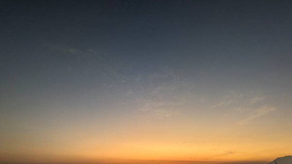 A tranquil sky with a vibrant gradient from dark blue to bright orange and yellow. The horizon is glowing with the warm light of sunrise, creating a peaceful atmosphere.