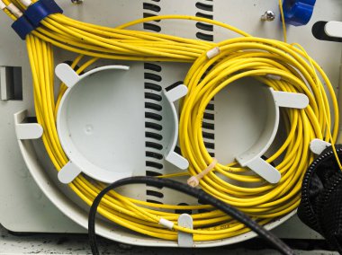 Beyaz plastik bir telekomünikasyon kablosu içinde düzgünce sarılmış ve emniyete alınmış sarı kablolar. Özellikler arasında iç kablo yönetim tepsileri, mavi klipler, bej kablo bağı ve siyah örgü yer alıyor..