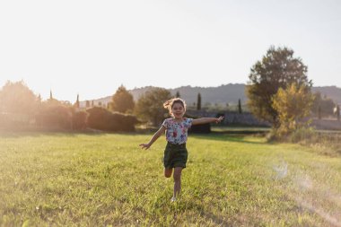 Gün batımında sahada koşan küçük bir çocuğun tam boy görüntüsü.