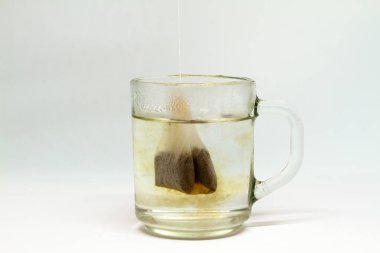 Beyaz arka planda çay poşeti olan cam bardak.