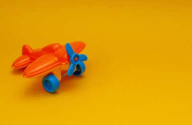 Sarı arka planda mavi pervaneli küçük turuncu oyuncak bir uçak.
