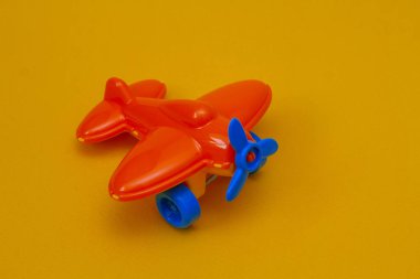 Sarı arka planda mavi pervaneli küçük turuncu oyuncak bir uçak.