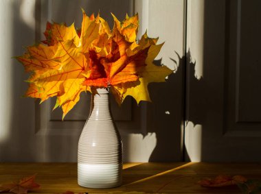 Akçaağaç yapraklı vazo ahşap masada.