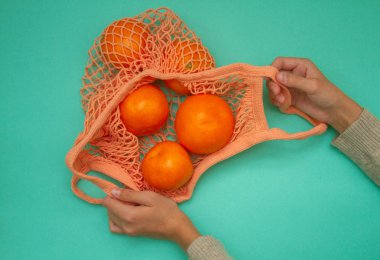 Turkuaz arka planda yeşil nane rengi tel torba içinde mandalinalar. Hasır bir torba içinde kağıt üzerinde turunçgil. Yukarıdan ateş edildi.