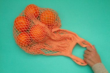 Turkuaz arka planda yeşil nane rengi tel torba içinde mandalinalar. Hasır bir torba içinde kağıt üzerinde turunçgil. Yukarıdan ateş edildi.