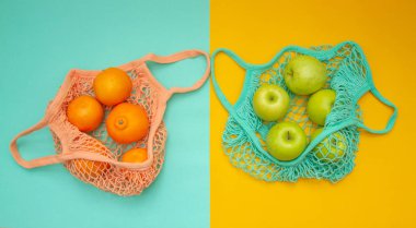 Kompozisyon yukarıdan iki yaprak üzerinde atılıyor - nane ve turuncu. Mandalina ve elmalı iki alışveriş torbası renkli bir arka planda yatıyor.. 