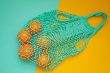 Turkuaz arka planda yeşil nane rengi tel torba içinde mandalinalar. Hasır bir torba içinde kağıt üzerinde turunçgil. Yukarıdan ateş edildi.