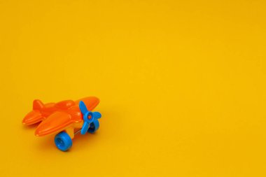 Sarı arka planda mavi pervaneli küçük turuncu oyuncak bir uçak.. 