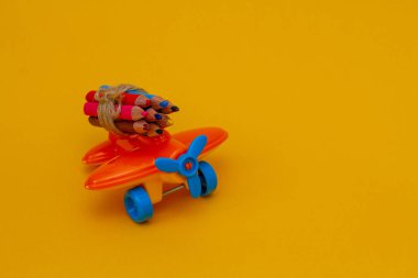 Sarı arka planda küçük bir oyuncak turuncu uçakta renkli kalemler.. 