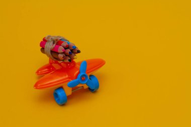 Sarı arka planda küçük bir oyuncak turuncu uçakta renkli kalemler.. 