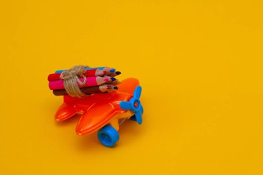 Sarı arka planda küçük bir oyuncak turuncu uçakta renkli kalemler.. 