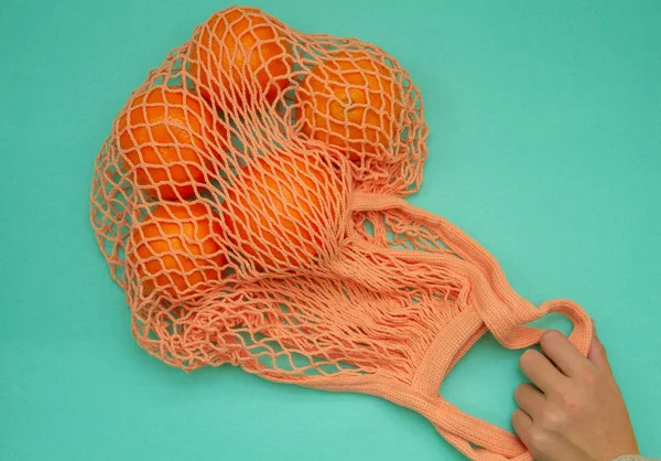 Tangerines in green mint color string bag on a turquoise background. Citrus in a wicker bag on paper. Shot from above.