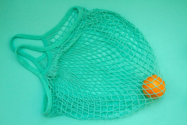 Mandarin in mint green string bag on a turquoise background. Citrus in a wicker bag on paper. Shot from above.