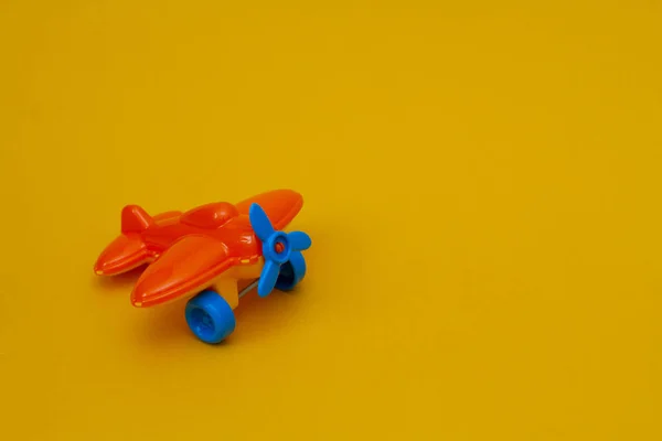 Small orange toy airplane with a blue propeller on a yellow background.