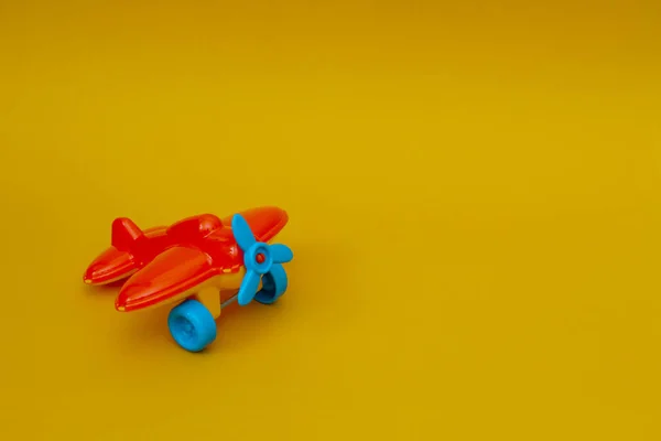 Small orange toy airplane with a blue propeller on a yellow background.