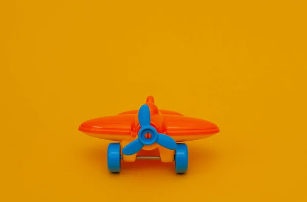 Small orange toy airplane with a blue propeller on a yellow background.